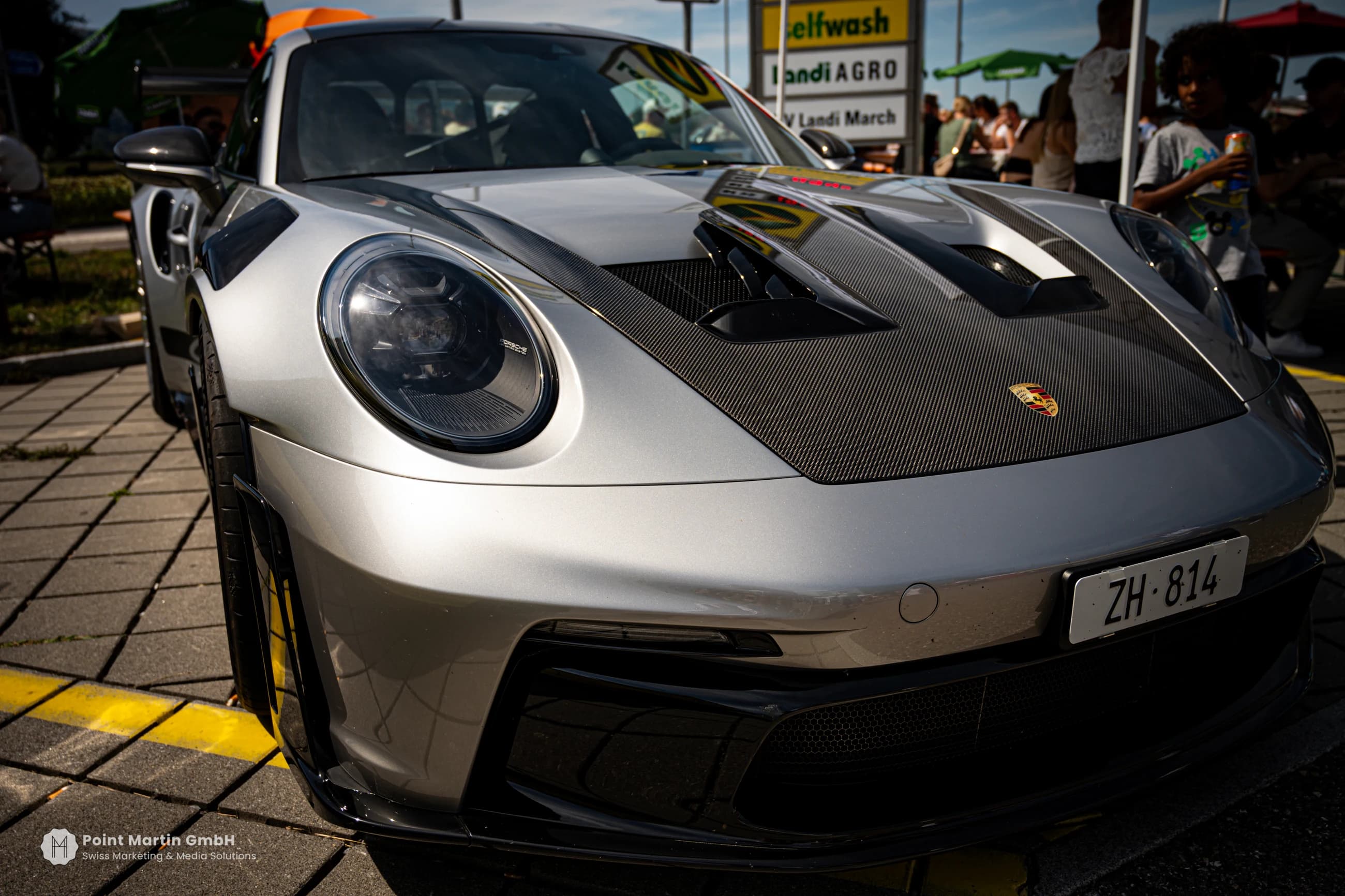 Silver Porsche viewed from the front, showing its round headlights and dark bonnet details